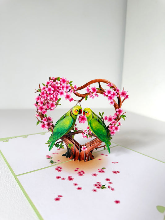 Pop-up card with two green parrots on a heart-shaped branch with pink flowers